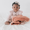 A baby girl sits up with a Clay Colored Lush Saranoni Blanket on her lap. The soft blanket is a small blanket and a baby blanket or toddler blanket.