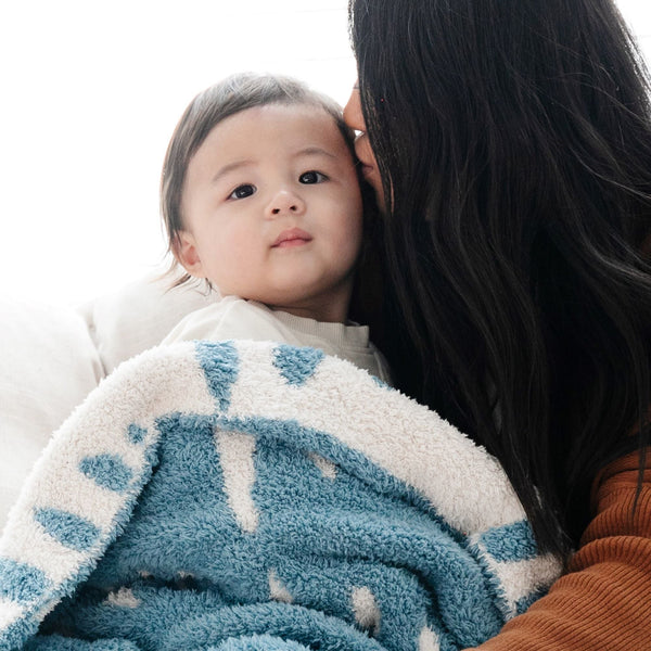 Mom kissing forehead of baby boy wrapped in blue Triangle DOUBLE-LAYER BAMBONI MINI BLANKETS - Saranoni