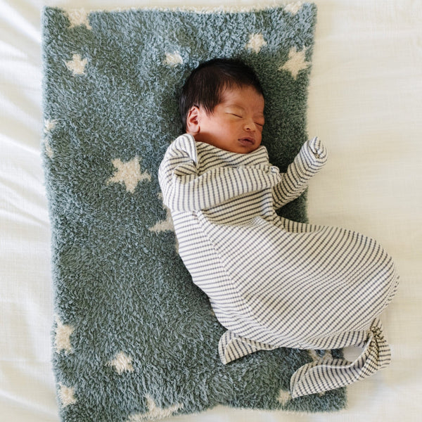 A baby boy lays on a double-layer Bamboni® baby blanket. The plush, breathable blanket features a two-tone blue and cream star design, offering ultimate softness and warmth. Made from Saranoni’s signature stretchy, cloud-like Bamboni® fabric, this luxury baby blanket provides comfort for naps, tummy time, and on-the-go snuggles. The perfect blend of warmth and breathability, it’s a must-have for parents seeking high-quality, ultra-soft blankets. The soft blanket is a mini blanket and Saranoni blanket. 