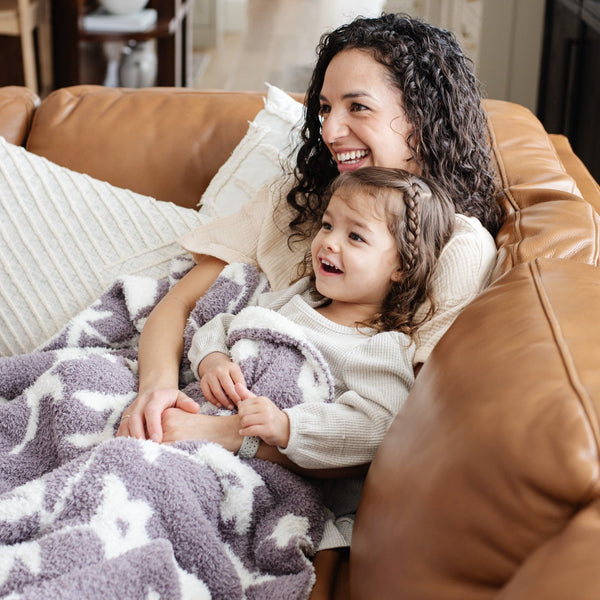 Mom and little daughter snuggling on the couch with adorable purple pansy DOUBLE-LAYER BAMBONI RECEIVING BLANKETS - Saranoni