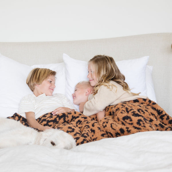 Three young siblings snuggling in bed with extra thick and cozy Classic Leopard DOUBLE-LAYER BAMBONI THROW BLANKETS - Saranoni