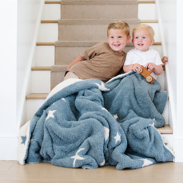 Two little boys sitting with each other on stairs, wrapped in Blue + White Stars Nightfall DOUBLE-LAYER BAMBONI TODDLER BLANKETS - Saranoni