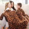 A mother and her son and daughter sit with a luxurious double-layer Bamboni® blanket by Saranoni, featuring classic leopard print of orange and black. This ultra-soft blanket is crafted from bamboo rayon and poly microfiber, making it lightweight, breathable, and fluffy. Ideal as a cozy blanket, extra large blanket, luxury blanket, soft blanket, or stylish home accent, this Saranoni blanket brings warmth, comfort, and timeless elegance to any living room or bedroom.