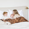 A little girl and her two brothers have a luxurious double-layer Bamboni® blanket by Saranoni, featuring classic leopard print of orange and black. This ultra-soft blanket is crafted from bamboo rayon and poly microfiber, making it lightweight, breathable, and fluffy. Ideal as a cozy blanket, extra large blanket, luxury blanket, soft blanket, or stylish home accent, this Saranoni blanket brings warmth, comfort, and timeless elegance to any living room or bedroom.