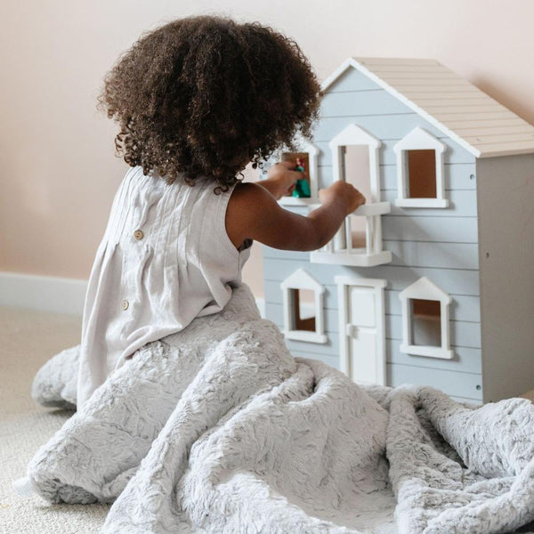 Girl playing with dollhouse and sitting with her DREAM TODDLER BLANKETS - Saranoni