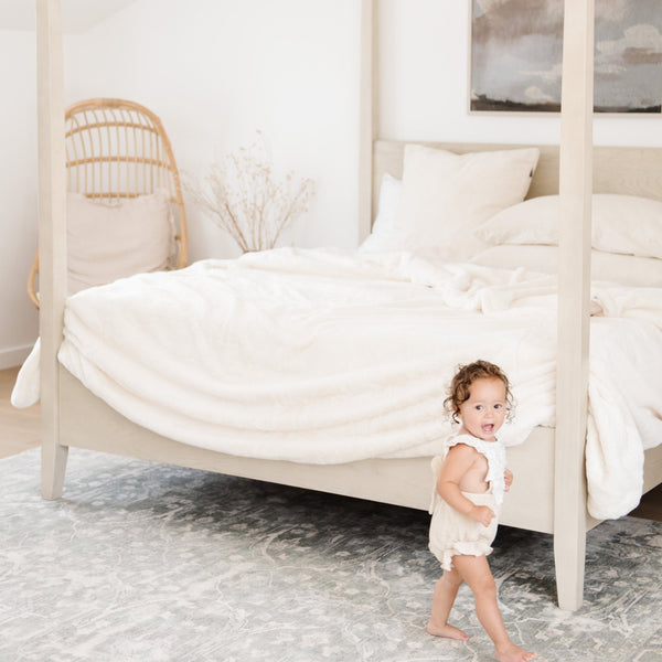 Little kid enjoying the warmth of a big fluffy Saranoni blanket on a bed.