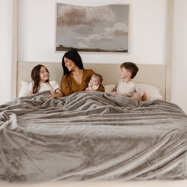 Family wrapped in a Saranoni blanket on a king-sized bed.