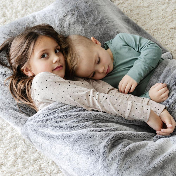 GRAND FAUX FUR SLEEPING BAGS - Kids lounging around in a gray mink sleeping bag, highlighting the signature Grand faux fur fabric.