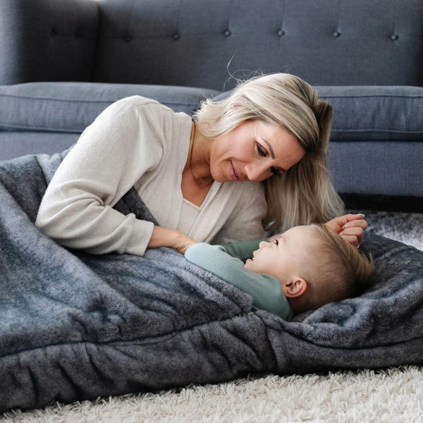 GRAND FAUX FUR SLEEPING BAGS - Little boy and his mom cuddling in a gray mink sleeping bag, highlighting the signature Grand faux fur fabric.