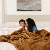 A little boy and his sister sit with a Saranoni Grand Faux Fur blanket, featuring an elegant golden tone and luxuriously soft texture. This cozy, extra large throw blanket and faux fur blanket offers soothing weight, premium softness, timeless comfort, and is a soft blanket. Perfect as a cozy blanket and luxury blanket for snuggling or as a luxury bedroom accent, this Saranoni blanket elevates every cozy moment and is a cozy blanket.