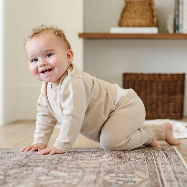 A baby boy crawls on a wooden floor. He is wearing a light tan, 100% cotton baby outfit that combines style and comfort. The Saranoni cloud-soft cotton set features a breathable waistband, loosely fitted sleeves, and elevated button details, making it perfect for everyday wear or special occasions. This heirloom-quality baby clothing offers timeless style and ultimate comfort. Ideal for parents searching for luxury baby clothes, soft cotton baby sets, or high-quality infant outfit.