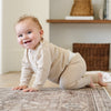 A baby boy crawls on a wooden floor. He is wearing a light tan, 100% cotton baby outfit that combines style and comfort. The Saranoni cloud-soft cotton set features a breathable waistband, loosely fitted sleeves, and elevated button details, making it perfect for everyday wear or special occasions. This heirloom-quality baby clothing offers timeless style and ultimate comfort. Ideal for parents searching for luxury baby clothes, soft cotton baby sets, or high-quality infant outfit.