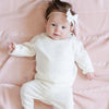 A baby girl lays on a Saranoni Heirloom Knit Blanket. She is wearing an all-white, 100% cotton baby outfit that combines style and comfort. The Saranoni cloud-soft cotton set features a breathable waistband, loosely fitted sleeves, and elevated button details, making it perfect for everyday wear or special occasions. This heirloom-quality baby clothing offers timeless style and ultimate comfort. Ideal for parents searching for luxury baby clothes, soft cotton baby sets, or high-quality infant outfit.