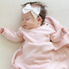 A baby girl lays on a Saranoni Heirloom Knit Blanket. She is wearing a light pink, 100% cotton baby outfit that combines style and comfort. The Saranoni cloud-soft cotton set features a breathable waistband, loosely fitted sleeves, and elevated button details, making it perfect for everyday wear or special occasions. This heirloom-quality baby clothing offers timeless style and ultimate comfort. Ideal for parents searching for luxury baby clothes, soft cotton baby sets, or high-quality infant outfit.