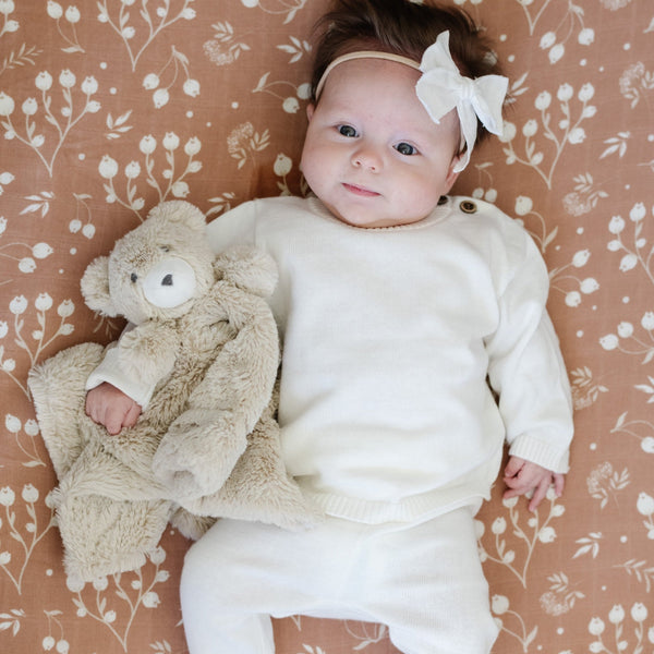 A baby girl lays on a Saranoni Blanket. She is wearing an all-white, 100% cotton baby outfit that combines style and comfort. The Saranoni cloud-soft cotton set features a breathable waistband, loosely fitted sleeves, and elevated button details, making it perfect for everyday wear or special occasions. This heirloom-quality baby clothing offers timeless style and ultimate comfort. Ideal for parents searching for luxury baby clothes, soft cotton baby sets, or high-quality infant outfit.