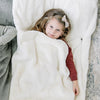 Little girl cuddles in her ivory faux fur sleeping bag. 