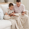 A father and son sit holding a Luxury Throw Buttermilk (light tan) Colored Lush Saranoni Blanket. The soft blanket is a throw blanket and has a soft faux fur feeling.