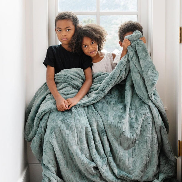 PATTERNED FAUX FUR XL THROW BLANKETS - Group of kids snuggling in a Saranoni blanket to keep them warm. 