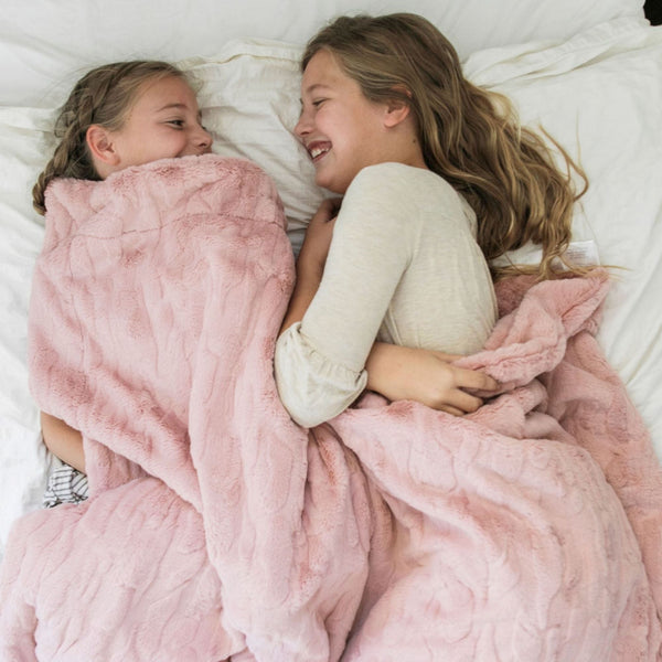 Two little girls hold a pink luxurious patterned faux fur extra large throw blanket that is a Saranoni blanket. This ultra-soft, cozy blanket adds a touch of elegance and warmth to any space, perfect as a soft oversized blanket or fluffy blanket for lounging. Ideal for those seeking a high-quality artificial fur blanket or luxury blanket, this versatile and stylish soft blanket enhances both comfort and decor. Shop the best blankets and throws for ultimate relaxation and cozy vibes.