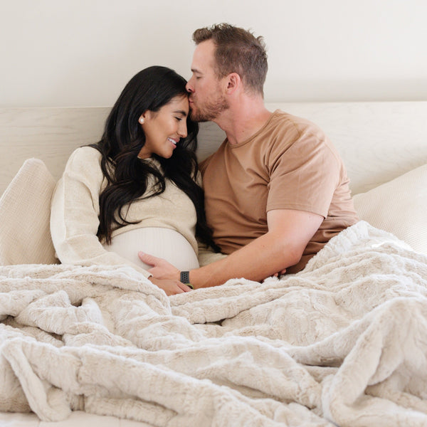 A husband and wife have a light tan  luxurious patterned faux fur extra large throw blanket that is a Saranoni blanket. This ultra-soft, cozy blanket adds a touch of elegance and warmth to any space, perfect as a soft extra large throw blanket or fluffy blanket for lounging. Ideal for those seeking a high-quality artificial fur blanket or luxury blanket, this versatile and stylish soft blanket enhances both comfort and decor. Shop the best blankets and throws for ultimate relaxation and cozy vibes.