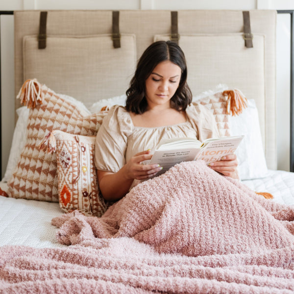 Woman reading a book in bed, snuggled with cozy Light Pink Cameo RIBBED BAMBONI KING BLANKETS - Saranoni