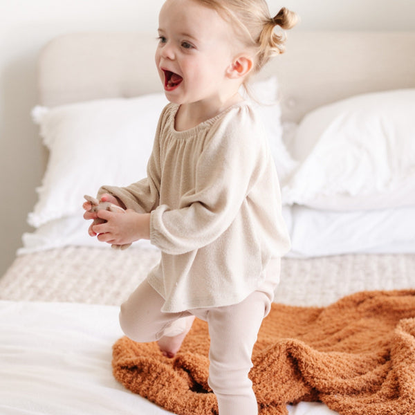 Little girl laughing and playing on bed with Orange Ginger RIBBED BAMBONI MINI BLANKETS - Saranoni