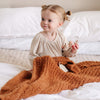 Little girl playing in bed with toys, laying with beautiful burnt orange Ginger RIBBED BAMBONI RECEIVING BLANKETS - Saranoni