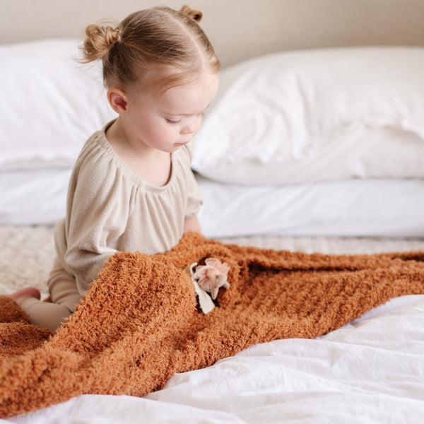 Little girl playing in bed with her favorite, extra stretchy burnt orange GingerRIBBED BAMBONI RECEIVING BLANKETS - Saranoni