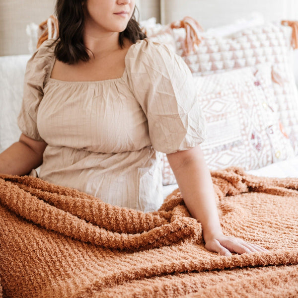 Woman feeling her beautiful and comfy orange Ginger RIBBED BAMBONI THROW BLANKETS - Saranoni