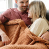 Wife and husband snuggling up together in their cozy orange Ginger RIBBED BAMBONI THROW BLANKETS - Saranoni