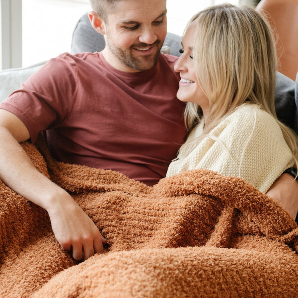 Husband and wife snuggled together in super soft and comfy orange Ginger RIBBED BAMBONI THROW BLANKETS - Saranoni