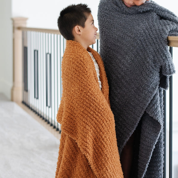 Young brothers both wrapped in super soft, stretchy and cozy burn orange Ginger + Charcoal RIBBED BAMBONI TODDLER BLANKETS - Saranoni