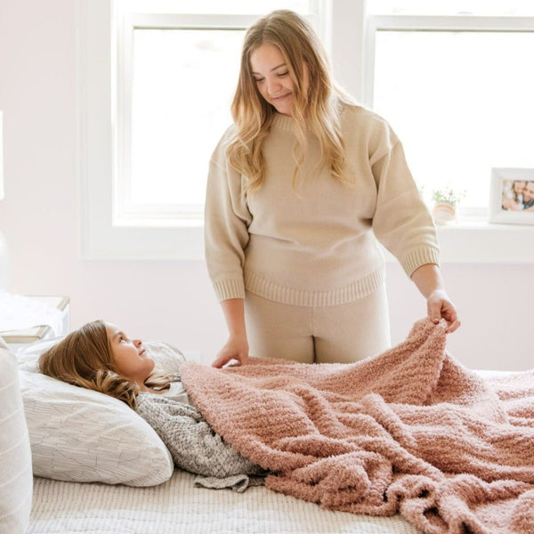 Mom putting daughter to bed with extra cozy and warm, light pink RIBBED BAMBONI TODDLER BLANKETS - Saranoni