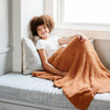 Little girl laying in reading nook, wrapped in beautiful and cozy burn orange Ginger RIBBED BAMBONI TODDLER BLANKETS - Saranoni