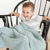 Adorable baby boy laughing on a rocking chair, sitting with extra soft and stretchy light blue Surf RIBBED BAMBONI TODDLER BLANKETS - Saranoni