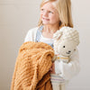 Smiling little girl holding stuffed lamb and extra soft Golden RIBBED BAMBONI TODDLER BLANKETS - Saranoni