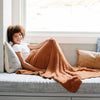 Girl sitting in window sill reading nook with her favorite super soft and warm burn orange Ginger RIBBED BAMBONI TODDLER BLANKETS - Saranoni