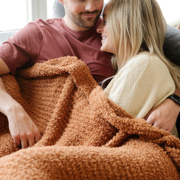 Husband and wife snuggling together in extra cozy and warm burnt orange Ginger RIBBED BAMBONI XL BLANKETS - Saranoni