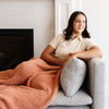 Woman sitting on the couch, cozied up with her favorite pink/peach Sunkissed RIBBED BAMBONI XL BLANKETS - Saranoni