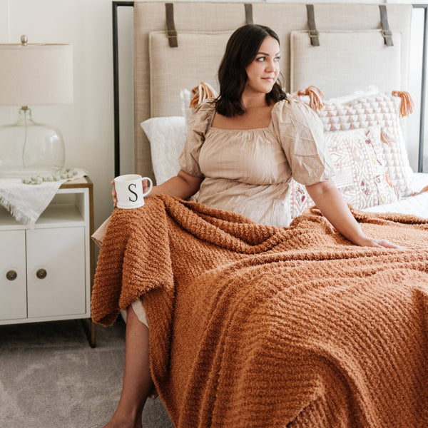 Woman sitting in bed with a beautiful, extra soft and stretchy burnt orange Ginger RIBBED BAMBONI XL BLANKETS - Saranoni