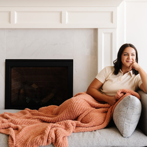 Woman sitting by the fireplace with her favorite super soft and stretchy pink/peach Sunkissed RIBBED BAMBONI XL BLANKETS - Saranoni