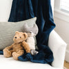 A Luxury Receiving Navy Colored Lush Saranoni Blanket is draped over a chair by some stuffed animals. The soft blanket is a small blanket and a baby blanket or toddler blanket.