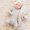 A Little Baby Girl with a White Bow and Gray Outfit hugging a Mini Saranoni Lush Blanket that is Feather Colored (similar to a light tan).