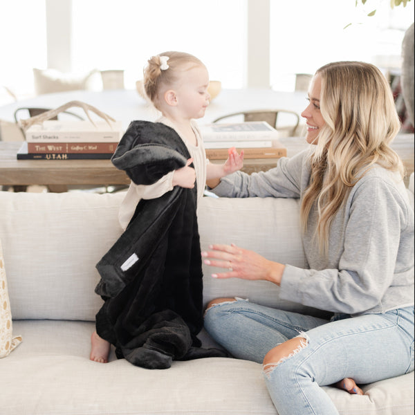 A little girl carries a Luxury Receiving Charcoal Colored Lush Saranoni Blanket. The soft blanket is a small blanket and a baby blanket or toddler blanket.