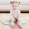 A little girl sits on a Dew (light blue) Colored Lush Saranoni Blanket. The soft blanket is a small blanket and a baby blanket or toddler blanket.