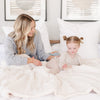 A mother and daughter sit with a Luxury Extra Large Oversized Throw Natural (off-white) Colored Lush Saranoni Blanket. The soft blanket is an extra large throw blanket and has a soft faux fur feeling.