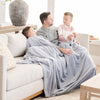 A father and his two sons sit while holding a Luxury Extra Large Oversized Throw Storm Cloud (dusty blue gray) Colored Lush Saranoni Blanket. The soft blanket is an extra large throw blanket and has a soft faux fur feeling.