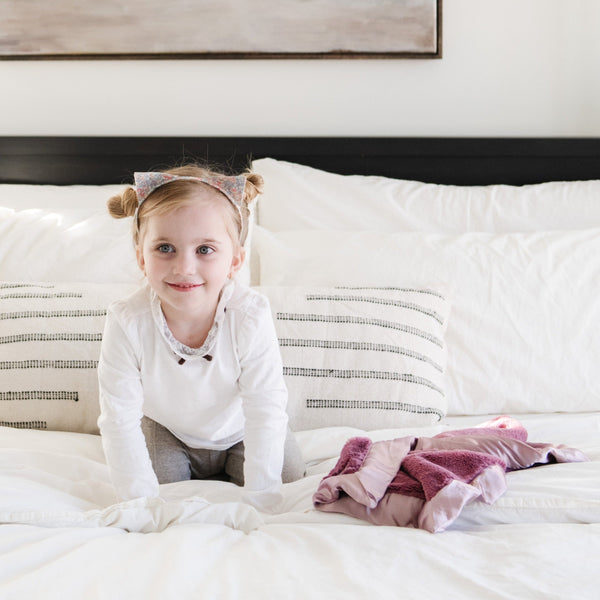 A young girl on a bed with a minky security blanket for babies and toddlers.