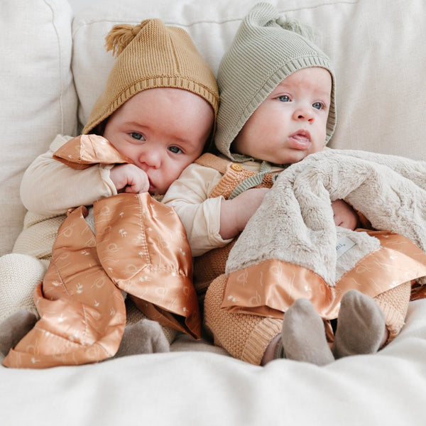 Two babies snuggled with cozy mini blankets with a satin back, offering a blend of plush warmth and the smooth, cooling feel of satin.