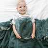 Little boy laying in bed with a cozy blue green toddler blanket. 